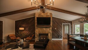 A spacious living room with a stone fireplace, leather furniture, and a large flat-screen TV. - Blue Ridge Haven is packed with luxury and family fun including a Hot Tub, Creekside Fire Pit, Game Room, Private Yard with Playset, and Back Deck with Grill. Your stay is owned and managed by a four time AirBnB Superhost. (Blue Ridge)