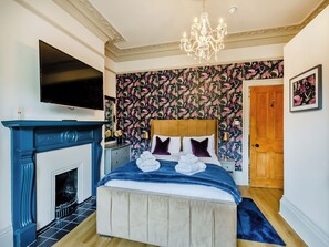 A bedroom with a bed, a television, a chandelier, a fireplace, and a door.