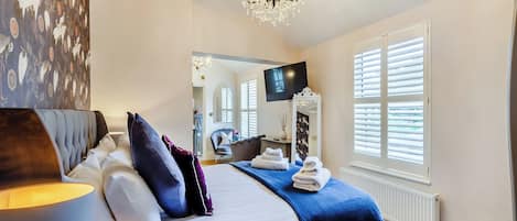 Une chambre d’hôtel moderne dotée d’un grand lit, d’un coin salon, d’une télévision et d’une grande fenêtre avec des stores.