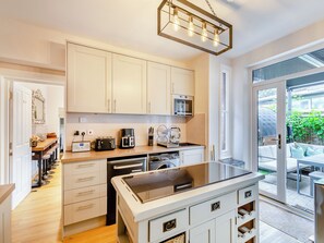 A modern kitchen with white cabinets, a built-in oven, a coffee maker, and a large island with a sink.