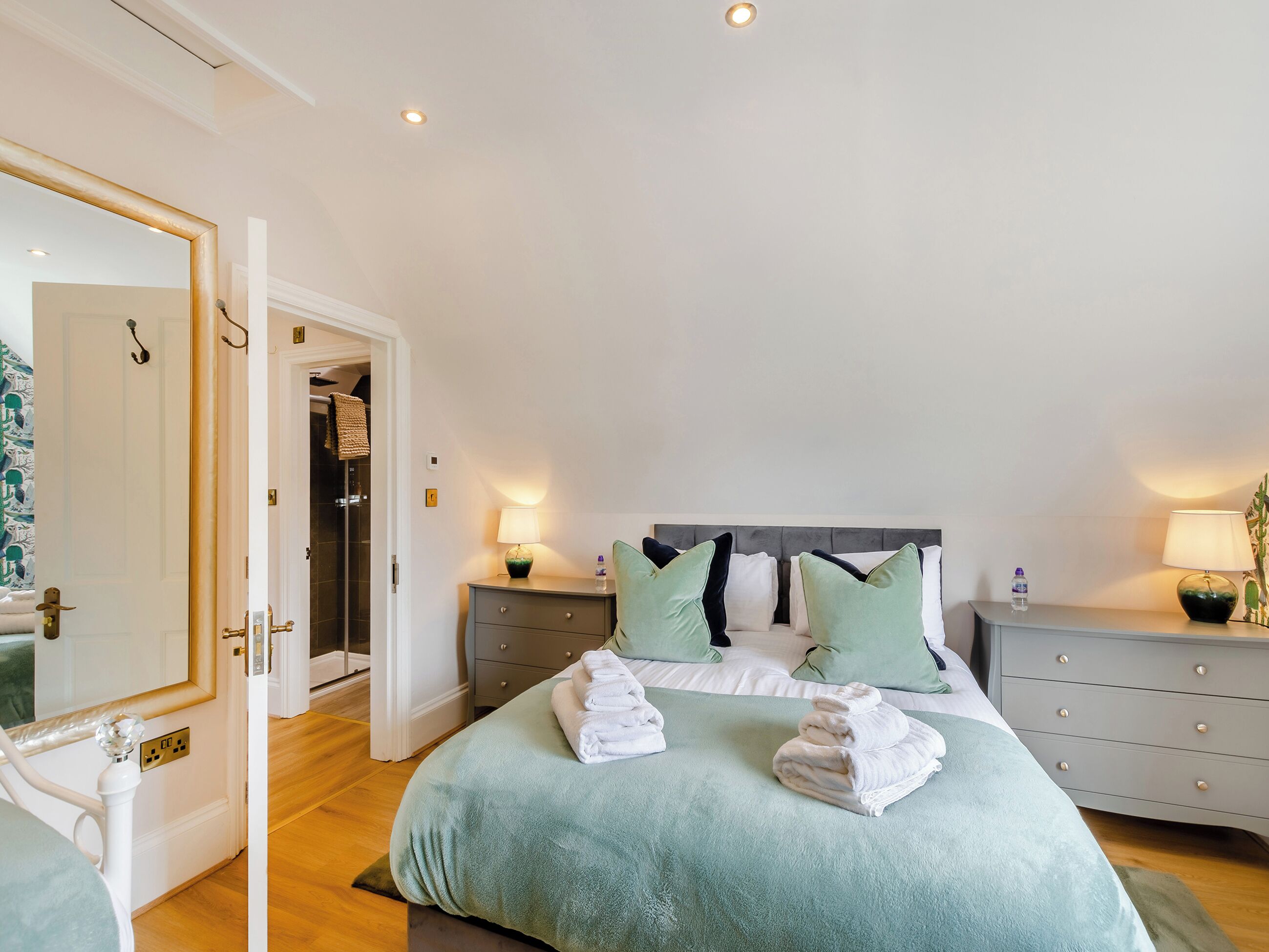 A neatly arranged bedroom with a bed, bedside tables, and a mirror.
