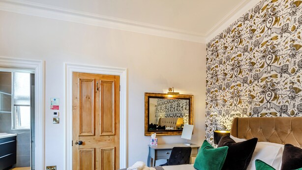 A hotel room with a large bed, a wooden door, a mirror, and a patterned wallpaper.