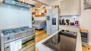 A modern kitchen with a gas stove, oven, and stainless steel range hood. There is a refrigerator with a built-in ice maker and a microwave. The kitchen has white cabinets and a wooden countertop.
