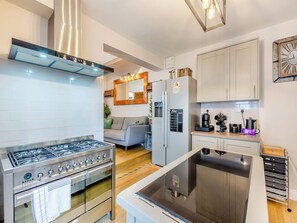 A modern kitchen with a gas stove, oven, and stainless steel range hood. There is a refrigerator with a built-in ice maker and a microwave. The kitchen has white cabinets and a wooden countertop. - 6 bedroom accommodation in York (York)