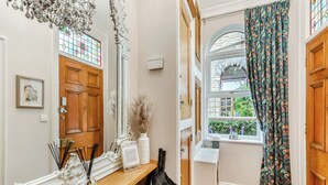 A hallway with a wooden door, a mirror, a radiator, and a window with patterned curtains.