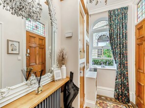 A hallway with a wooden door, a mirror, a radiator, and a window with patterned curtains. - 6 bedroom accommodation in York (York)