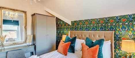 A hotel room with a bed, a chandelier, a wardrobe, and a colorful floral wallpaper.