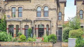 A Victorian-style brick house with multiple windows, a chimney, and a garden with various plants and flowers.
