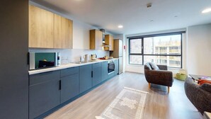 A modern kitchen with grey cabinets, a built-in oven, and a large window offering a view of the city. - Student Only Canvas Walthamstow in London (London)