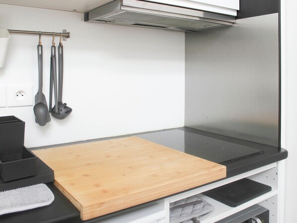 Una cocina con tabla de madera, encimeras negras y utensilios de cocina colgantes.