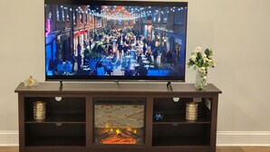 A television on a wooden console with decorative items and a small fireplace. - A luxurious getaway in beautiful Buford. (Buford)
