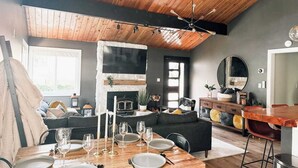 A modern living room with a fireplace, wooden ceiling, and a dining area set for a meal. - Fully Remodeled Home Away From Home with all the amenities (Sugarloaf)