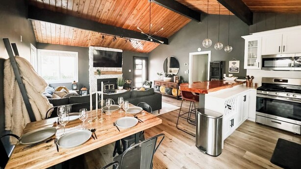 A spacious kitchen with wooden flooring, a dining area with a wooden table set for four, and a modern kitchen island. - Fully Remodeled Home Away From Home with all the amenities (Sugarloaf)