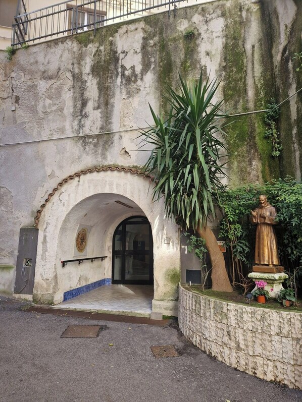 A building entrance with a stone archway, a statue, and a potted plant.