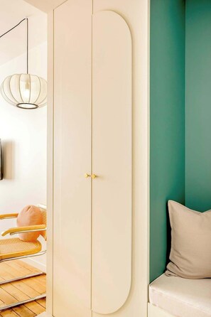 Quarto com guarda-roupa branco, parede em tom de verde-água, cadeira de vime e sofá branco.