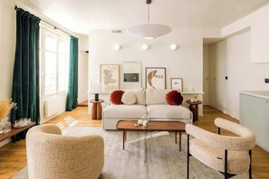 Uma sala de estar moderna com um sofá branco, duas poltronas, uma mesa de centro e um lustre.