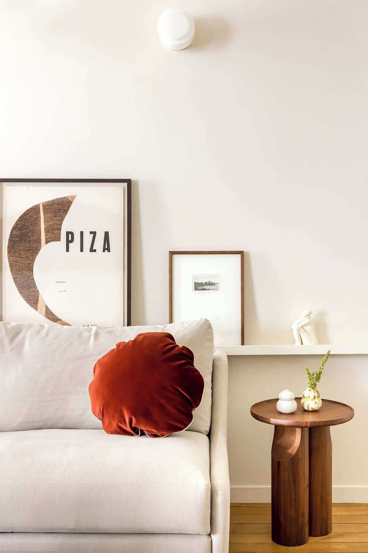 Una sala de estar moderna con un sofá blanco, un cojín rojo, un letrero de pizza enmarcado y una pequeña mesita de madera con adornos.