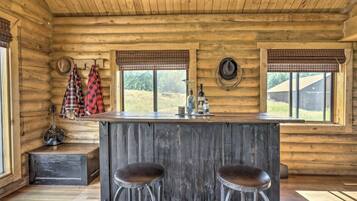 A rustic wooden cabin interior with a bar area, two stools, and a guitar.