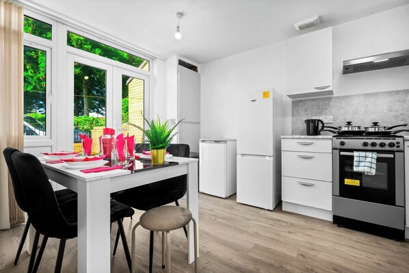 A modern kitchen with white cabinetry, a gas stove, a refrigerator, and a dining area with a table set for two.