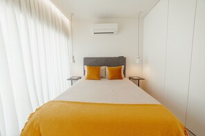 Habitación de hotel con cama, dos mesitas de noche, unidad de aire acondicionado y ventana con cortinas.