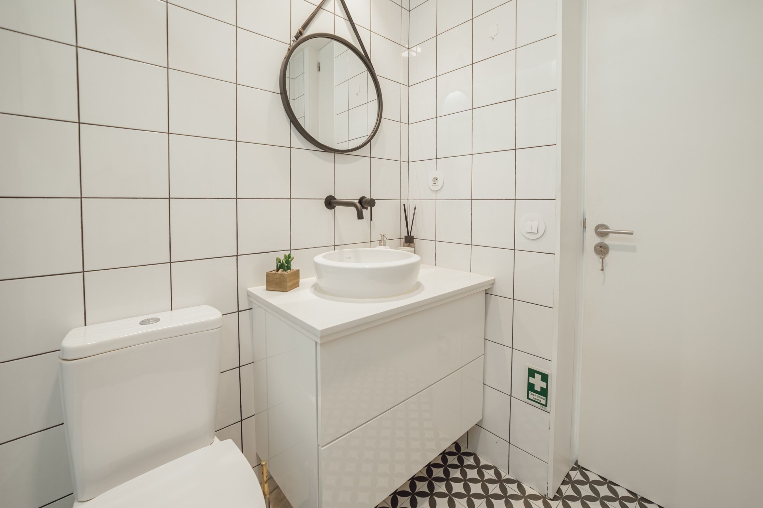 Een badkamer met witte tegels, een witte wastafel, een toilet en een spiegel.