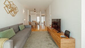 A modern living room with a grey sofa, a wooden TV stand, and a dining area in the background. - Porto Panoramic Views With Terrace by Vacationy (Porto)