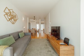 A modern living room with a grey sofa, a wooden TV stand, and a dining area in the background. - Porto Panoramic Views With Terrace by Vacationy (Porto)