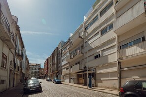 Una estrecha calle empedrada flanqueada por edificios de varios pisos, algunos con balcones y escaparates.