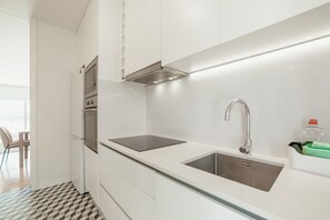 Una cocina moderna con armarios blancos, un lavamanos de acero inoxidable y una campana extractora empotrada.