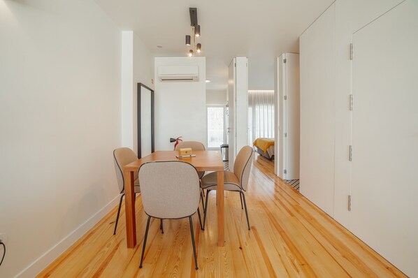 A modern dining area with a wooden table and chairs, an air conditioning unit, and a view into another room.