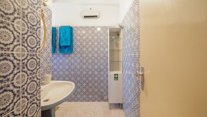 Une salle de bain avec des carreaux à motifs, un lavabo, un miroir et un meuble surmonté d’une enseigne verte.