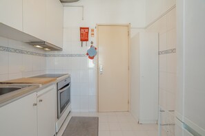 A kitchen with white tiles, a wooden countertop, an oven, and a door with a red sign.