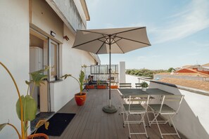 Een balkon met een tafel, stoelen, een potplant en een grote parasol.