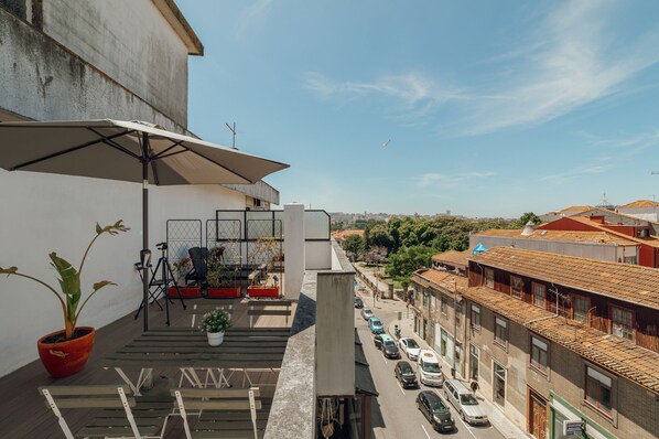 A balcony with a potted plant, outdoor furniture, and a view of a city street.