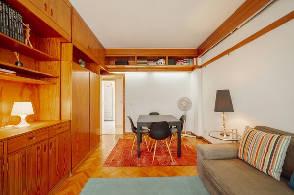 Um espaço compacto com área de jantar, um sofá e uma mesinha com abajur.