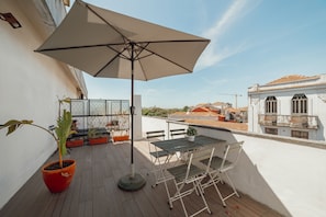 En udendørs terrasse med et bord, stole, en potteplante og en parasol.