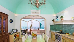 Una cucina con zona pranzo, vista attraverso un'ampia finestra e un lampadario.
