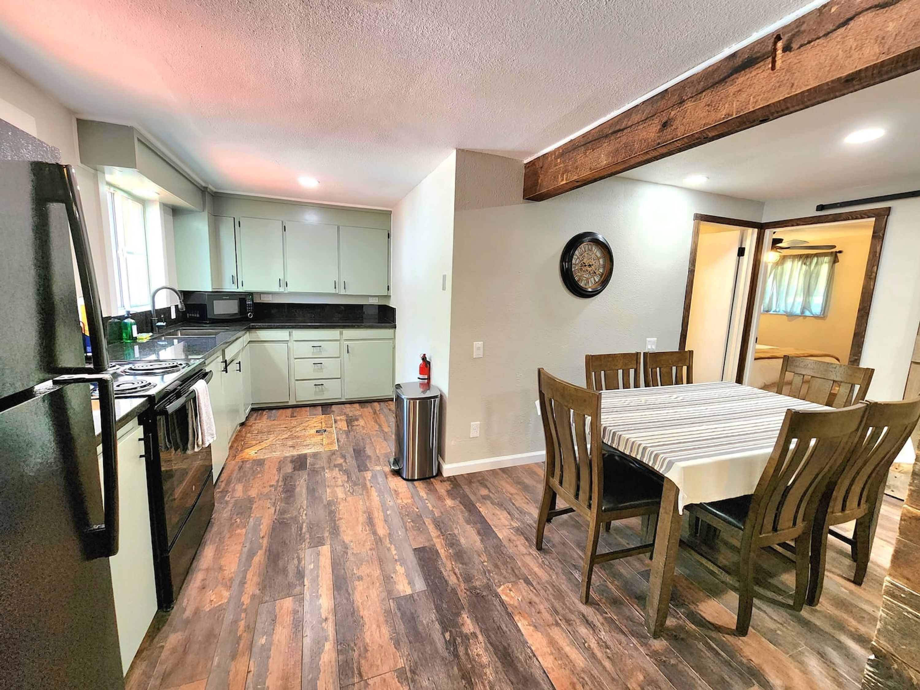 A kitchen with a dining area, wooden flooring, and a clock on the wall.