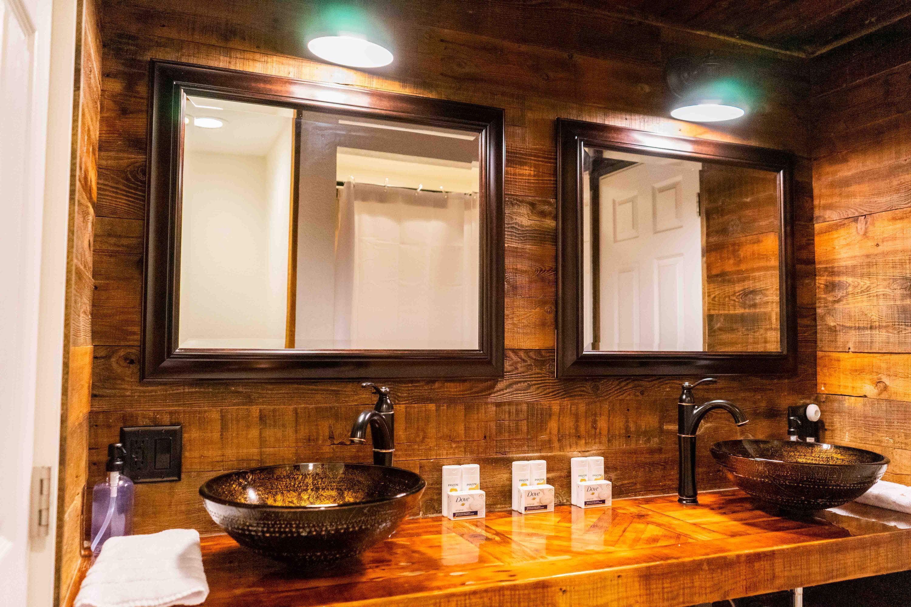 A wooden bathroom vanity with two sinks, each with a vessel basin and a mirror above.