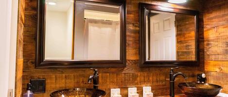 A wooden bathroom vanity with two sinks, each with a vessel basin and a mirror above.