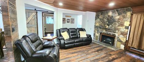 A living room with a stone fireplace, leather sofas, and a ceiling fan.