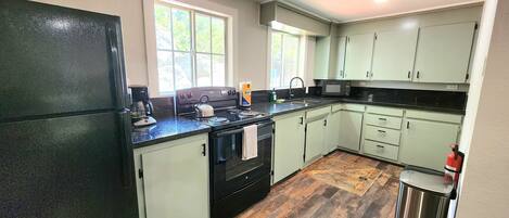 A kitchen with a black refrigerator, a stove, and a microwave. There is a window with a view of trees outside.
