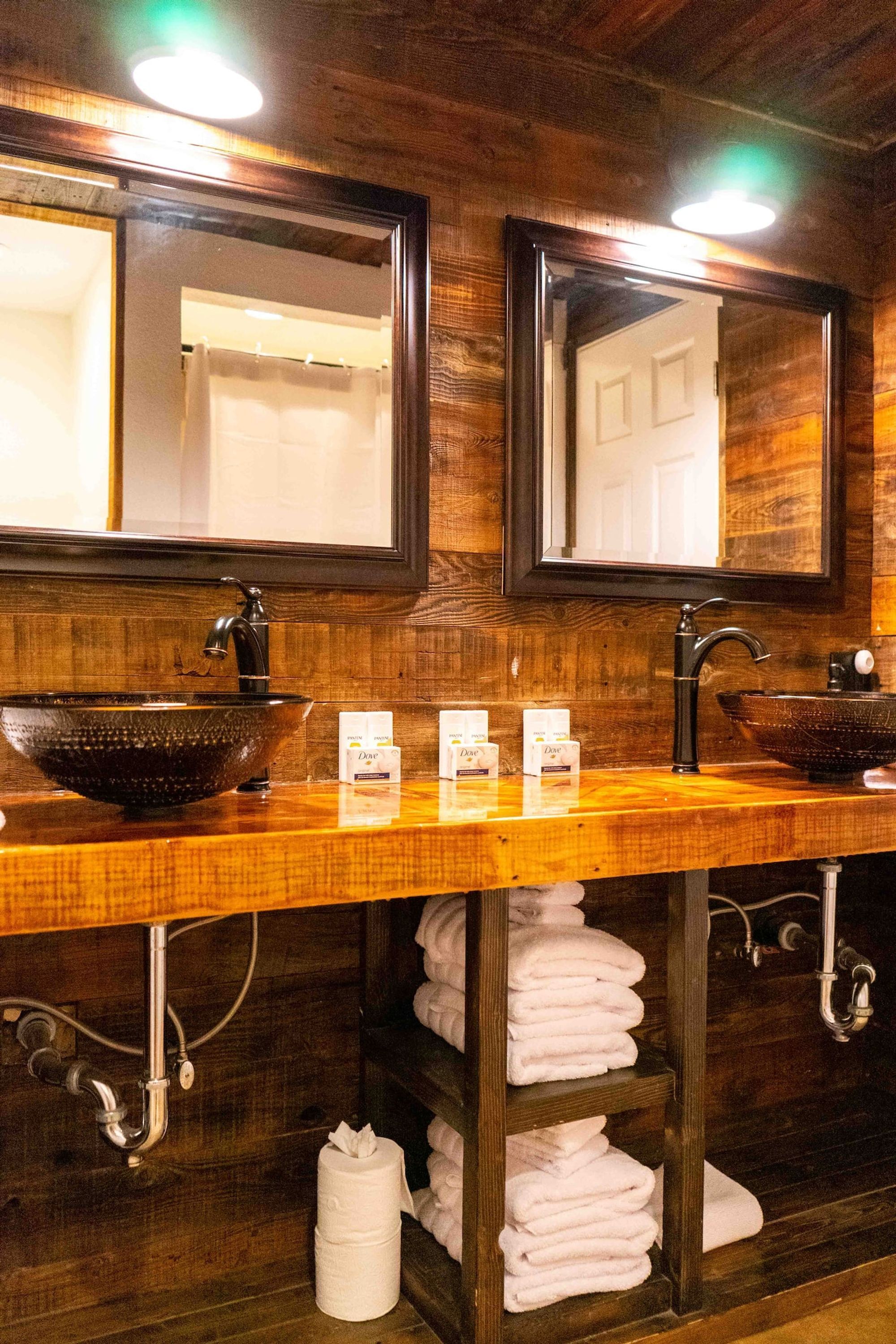 A wooden vanity with two sinks, a large mirror, and a towel rack with folded towels.