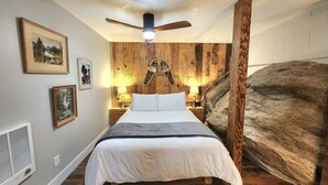 Um quarto com cama, paredes de madeira, ventoinha no teto e quadros nas paredes.