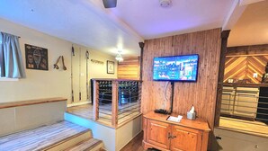 Um saguão de hotel com uma escada de madeira, um balcão de recepção, uma televisão fixada na parede e um suporte na parede com varas de pesca.