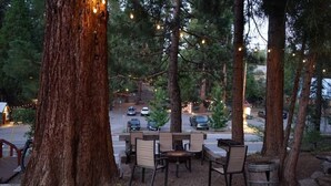 An outdoor seating area with tables and chairs under trees, surrounded by a gravel ground. - Fox Den Suite in Shaver Lake (Shaver Lake)
