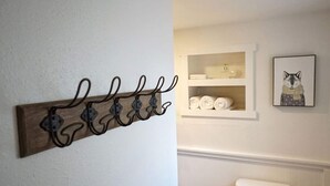 A bathroom with a wooden wall-mounted rack holding towels, a shelf with toiletries, and a framed picture of a fox. - Fox Den Suite in Shaver Lake (Shaver Lake)
