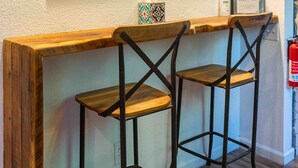 Un coin bar avec deux tabourets, des œuvres d’art encadrées accrochées au mur et une petite table sur laquelle se trouvent une bouteille et une boîte de mouchoirs.