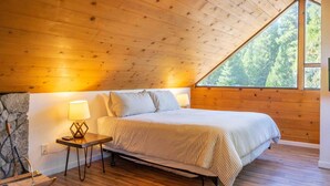 Une chambre à coucher aux murs lambrissés, avec un lit, une table de chevet, une lampe et une grande fenêtre.
