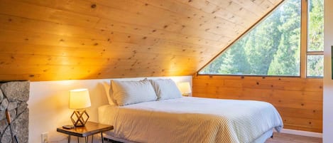 Une chambre à coucher aux murs lambrissés, avec un lit, une table de chevet, une lampe et une grande fenêtre.